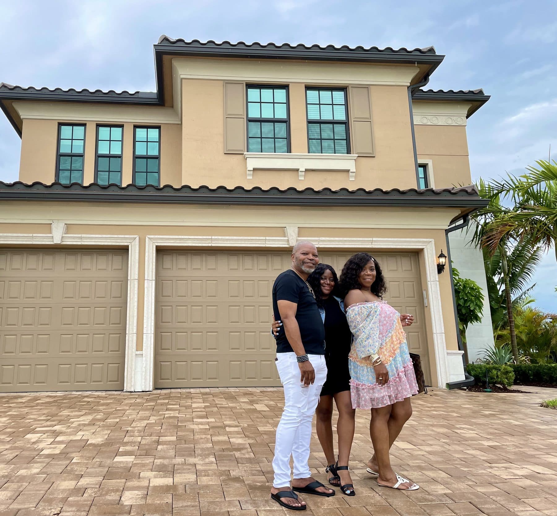 Clients smiling in front of a two-story South Florida home on closing day