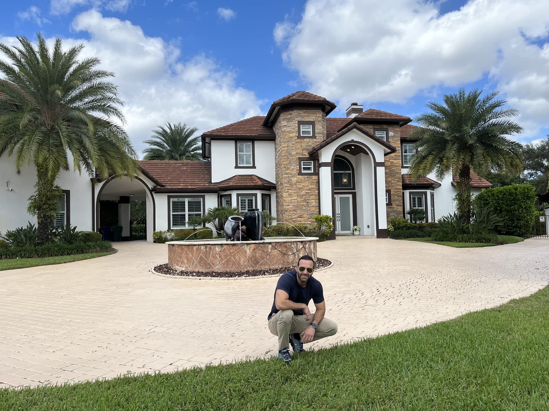 A client crouching on the lawn in front of a home with palm trees on closing day