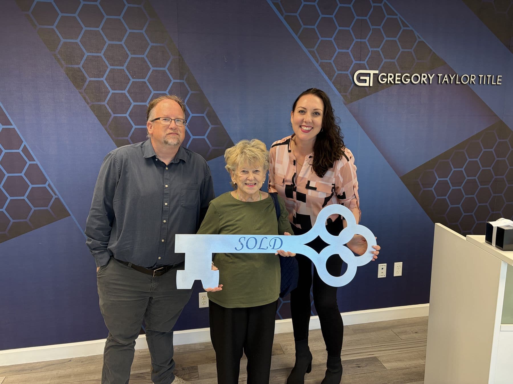 Crystal Creed with two clients holding a Sold key sign at the title office