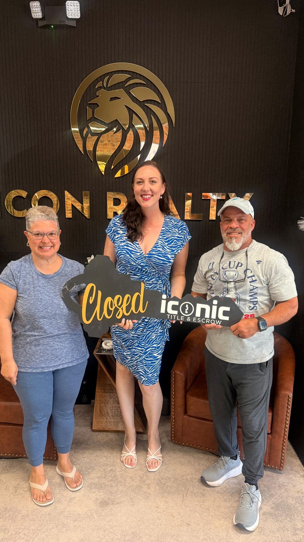 Crystal Creed with two clients holding a Closed key sign at the Icon Realty office